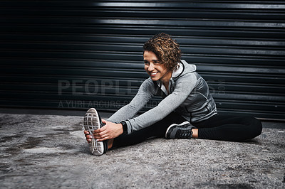 Buy stock photo Full length shot of an attractive young woman sitting and stretching her legs before her workout outside
