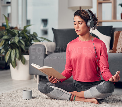 Buy stock photo Full length shot of an attractive young woman sitting and listening to music while reading in her living room