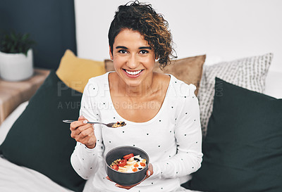 Buy stock photo Cropped portrait of an attractive young woman holding a bowl of oats while sitting on her bed at home