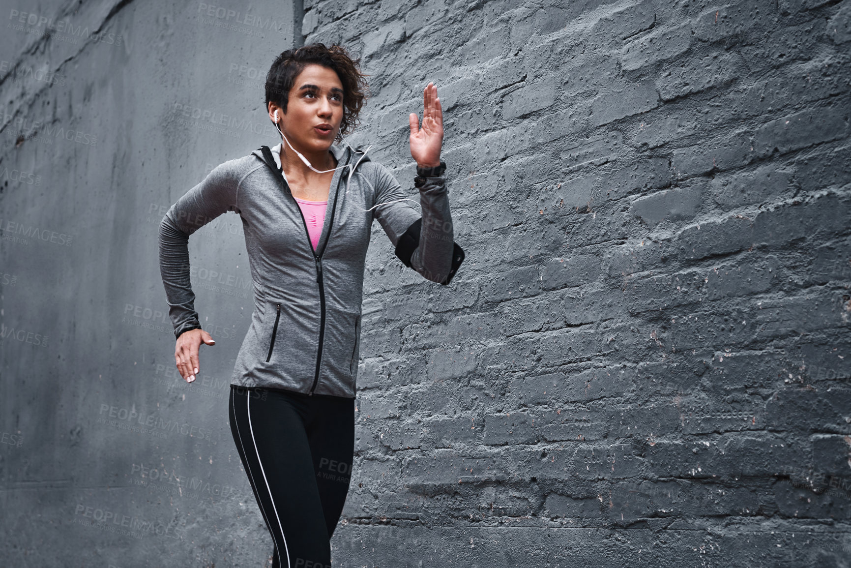Buy stock photo Cropped shot of an attractive young woman wearing earphones and workout clothes while running outside