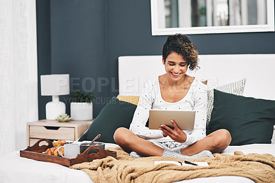 Buy stock photo Full length shot of an attractive young woman sitting on her bed and using her tablet while at home