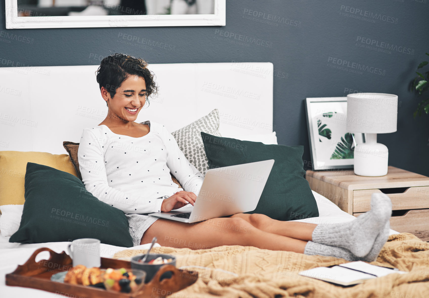 Buy stock photo Full length shot of an attractive young woman sitting on her bed and using a laptop before eating breakfast