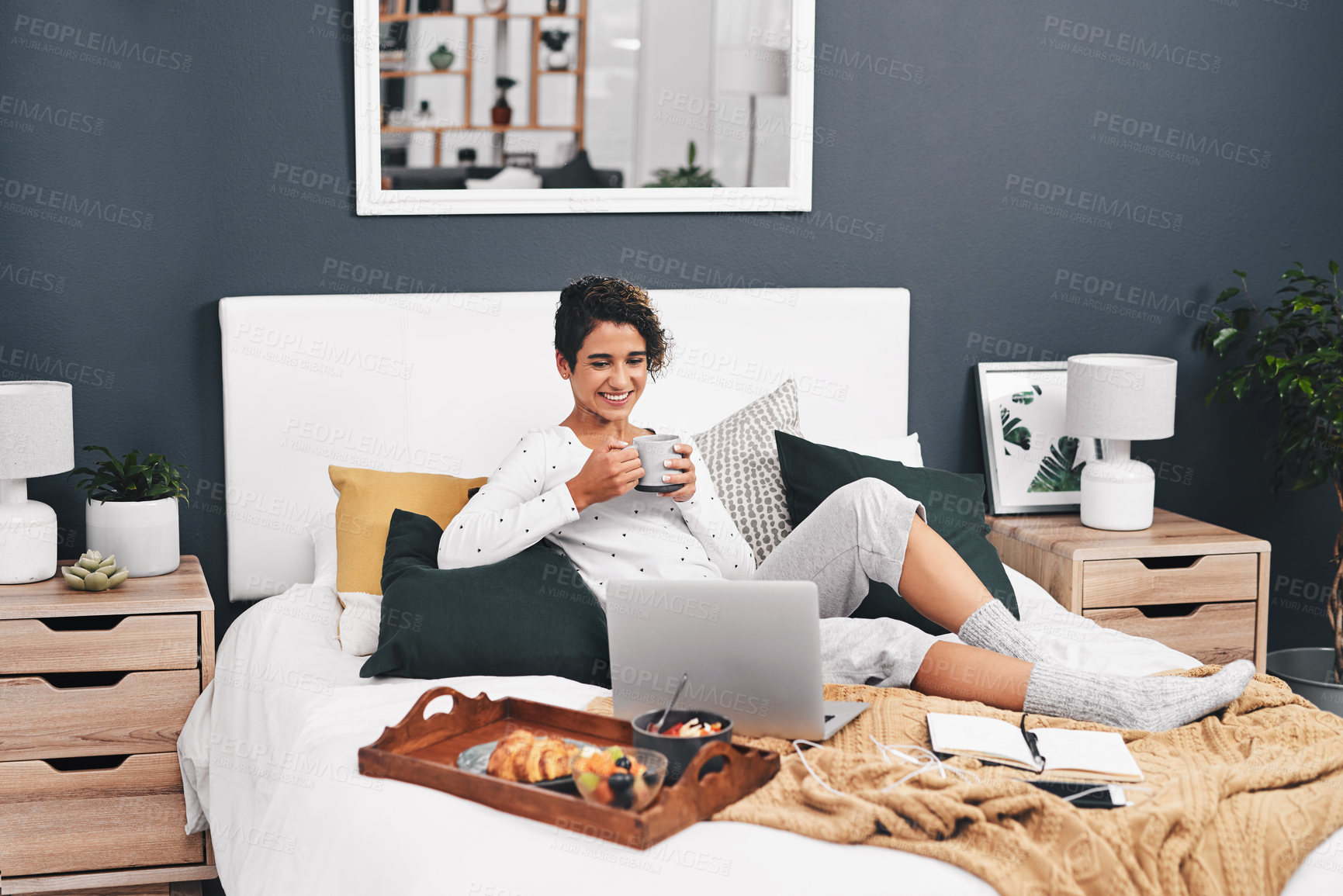 Buy stock photo Full length shot of an attractive young woman enjoying breakfast in bed while using her laptop at home