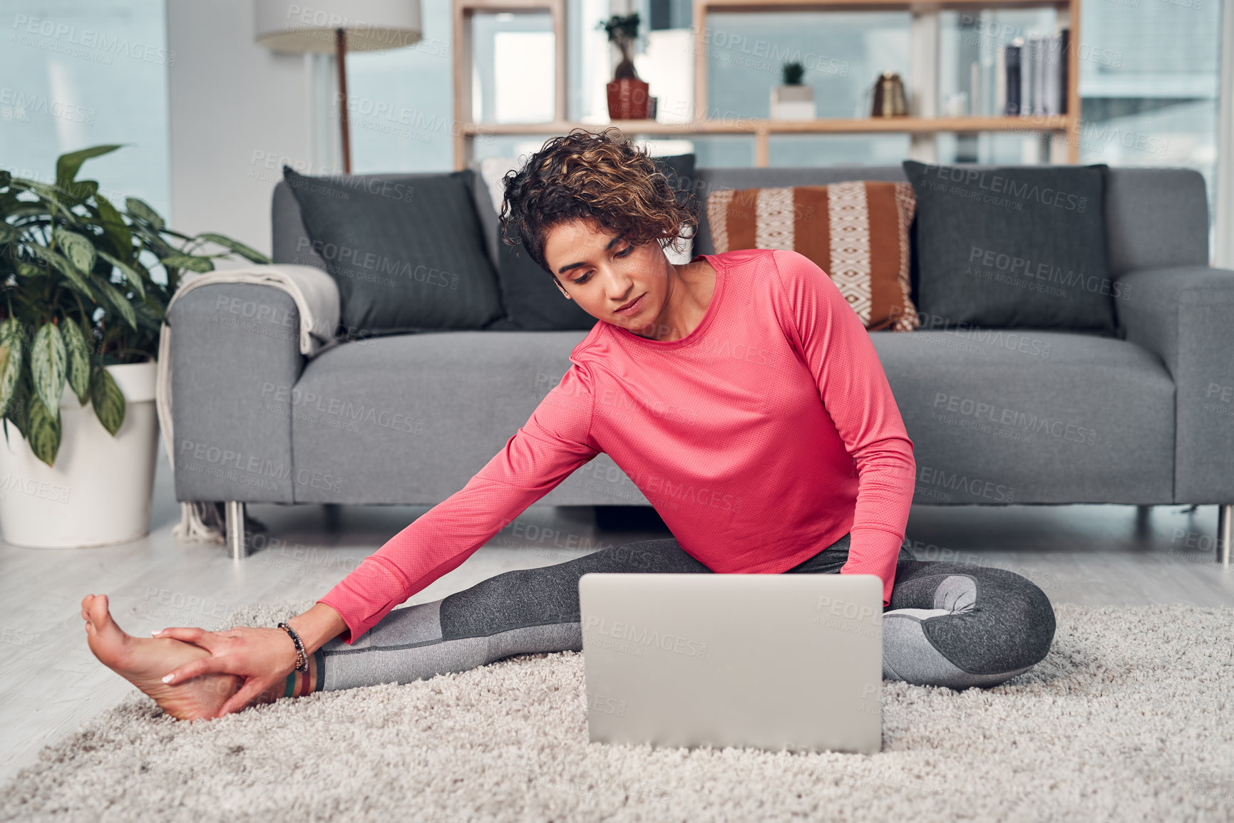 Buy stock photo Full length shot of an attractive young woman multitasking and using a laptop while stretching in her living room