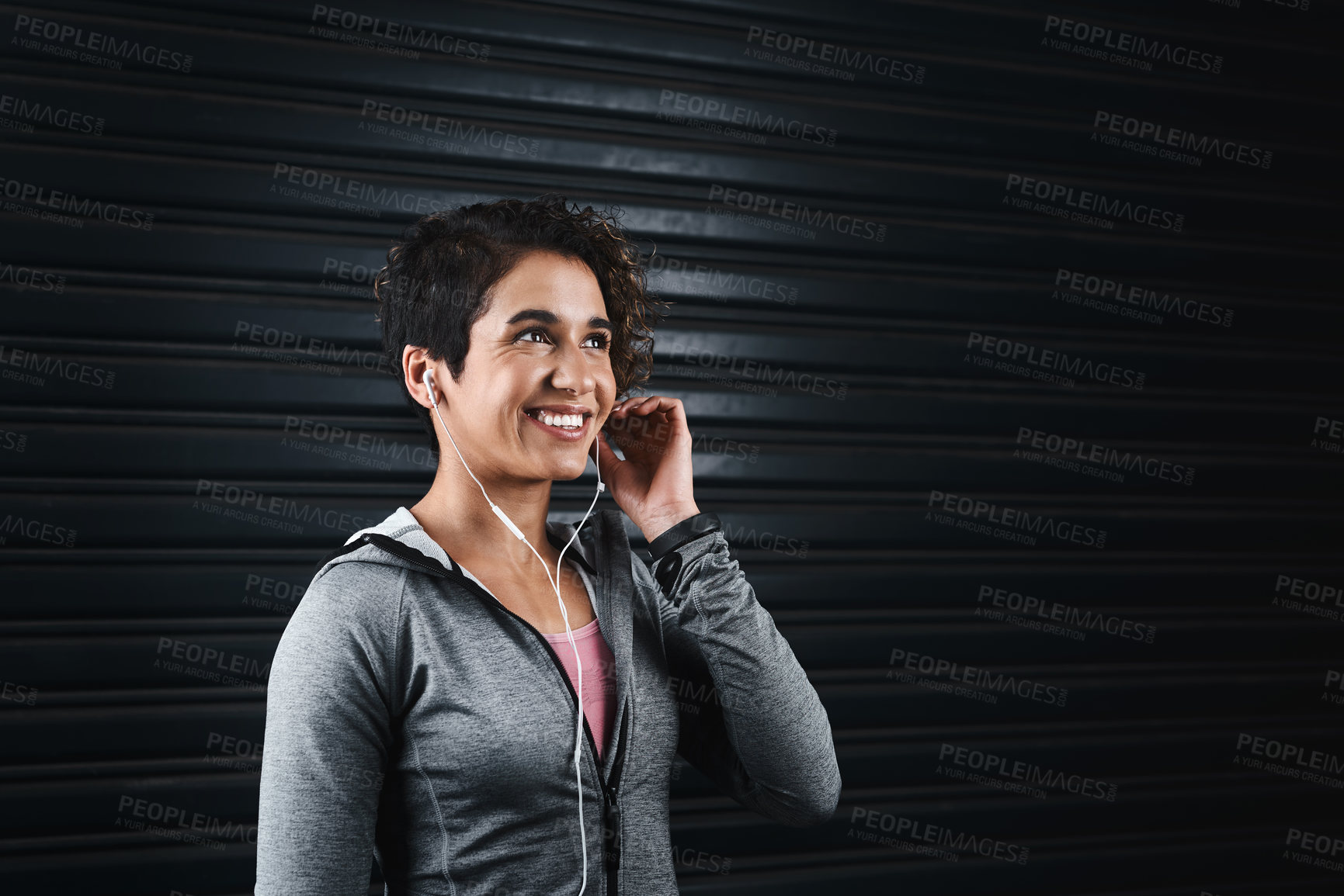 Buy stock photo Cropped shot of an attractive young woman wearing earphones and standing against a black background before exercising