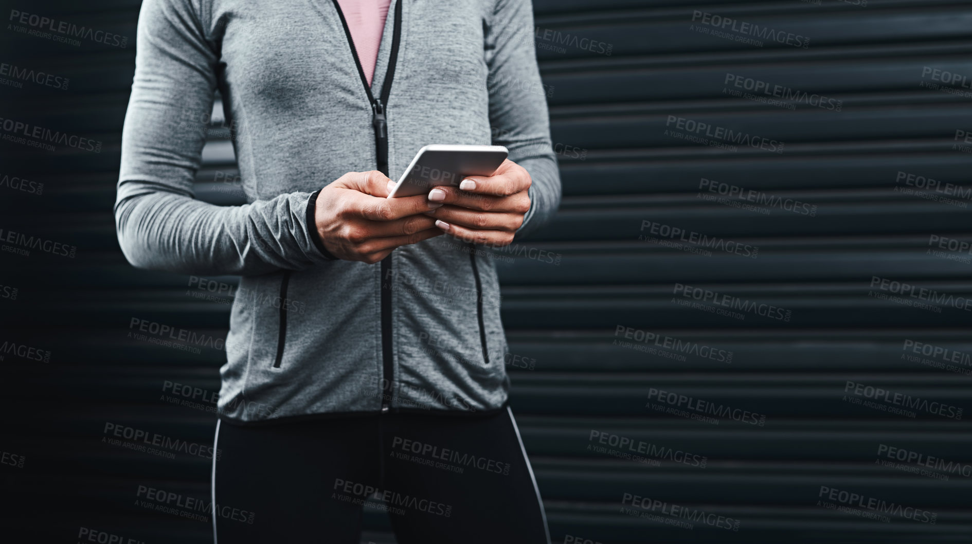Buy stock photo Cropped shot of an unrecognizable woman standing against a black background and using her cellphone after her workout