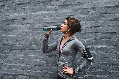 Buy stock photo Cropped shot of an attractive young woman listening to music and drinking water after working out while outside