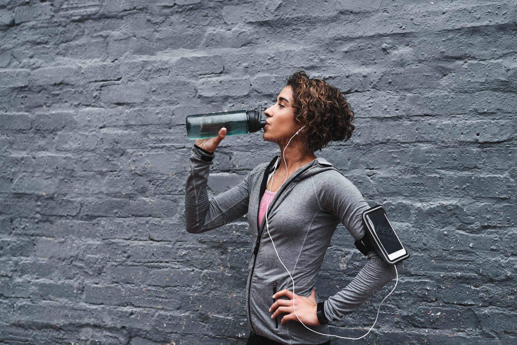 Buy stock photo Cropped shot of an attractive young woman listening to music and drinking water after working out while outside
