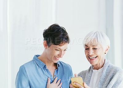 Buy stock photo Cropped shot of a senior woman holding a cellphone while talking with her attractive young daughter while at home
