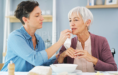 Buy stock photo Cropped shot of an attractive young woman wiping her senior mother's mouth while they have breakfast together at home