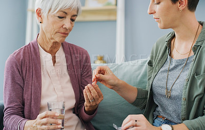 Buy stock photo Cropped shot of an attractive young woman giving her sick senior mother painkillers while sitting with her on the sofa