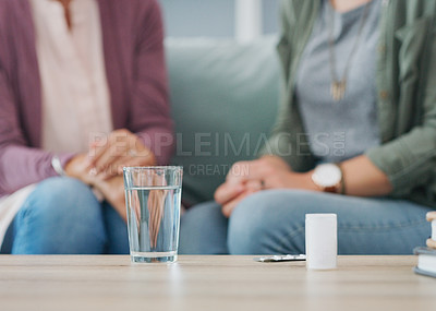 Buy stock photo Cropped shot of two unrecognizable women sitting on the sofa with a pillbox and water in the living room