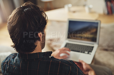 Buy stock photo Rearview shot of a handsome young man using his laptop while relaxing on a couch at home