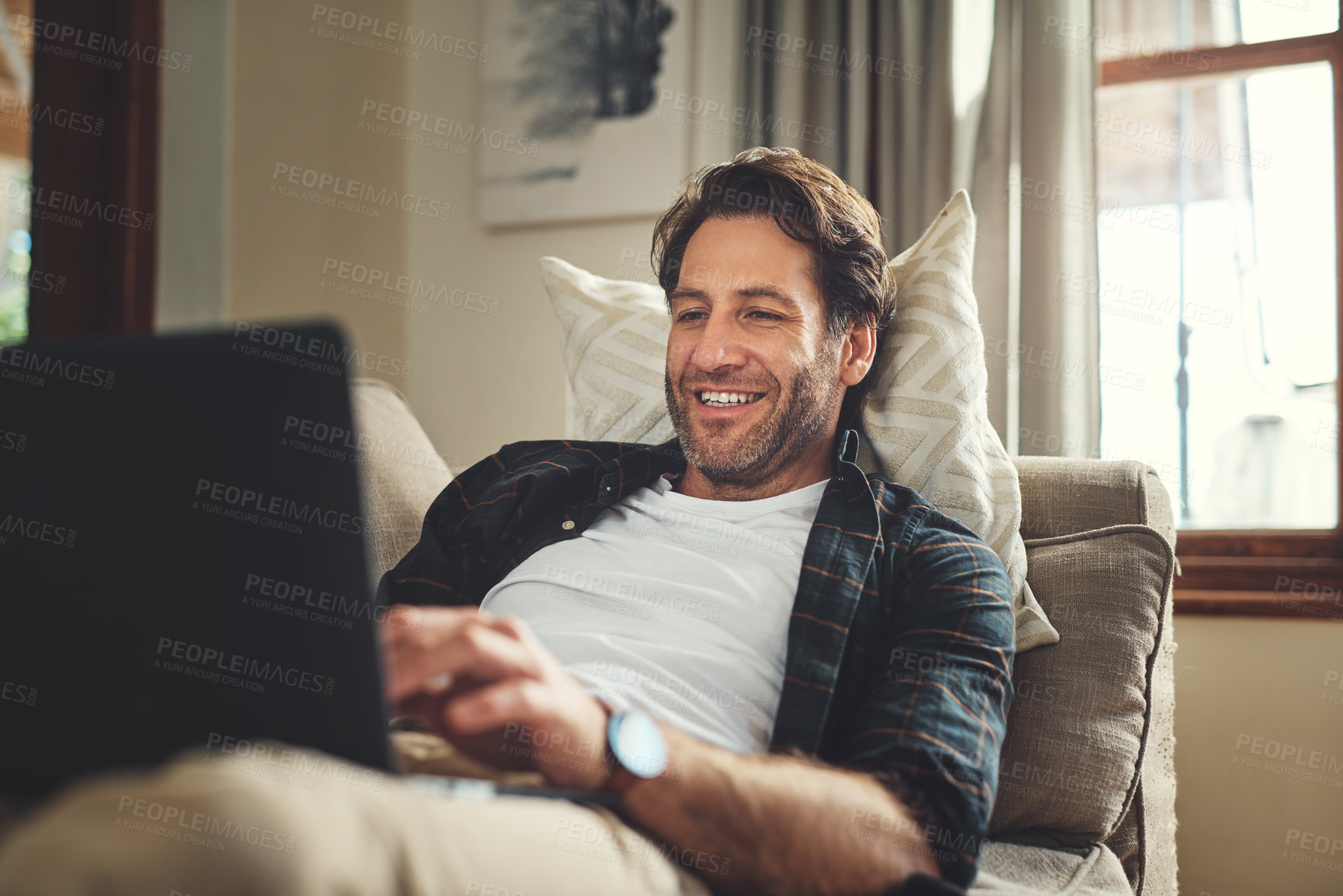 Buy stock photo Laptop, smile and man in home for relax, reading email and social media. Computer, remote work and freelance journalist in living room for writing article, research report or news on internet on sofa