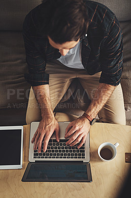 Buy stock photo High angle shot of a handsome young man using his laptop while relaxing on a couch at home