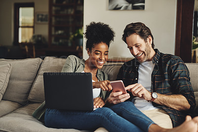 Buy stock photo Shot of a happy young couple using a laptop and cellphone while relaxing on a couch home
