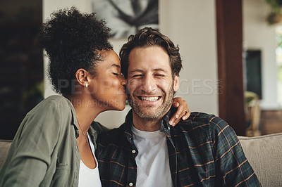 Buy stock photo Shot of a young woman kissing her boyfriend on the cheek while relaxing on a sofa at home