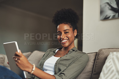Buy stock photo Shot of a beautiful young woman using a digital tablet while relaxing on her sofa at home