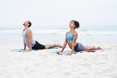 Buy stock photo Shot of a young man and woman practising yoga together at the beach