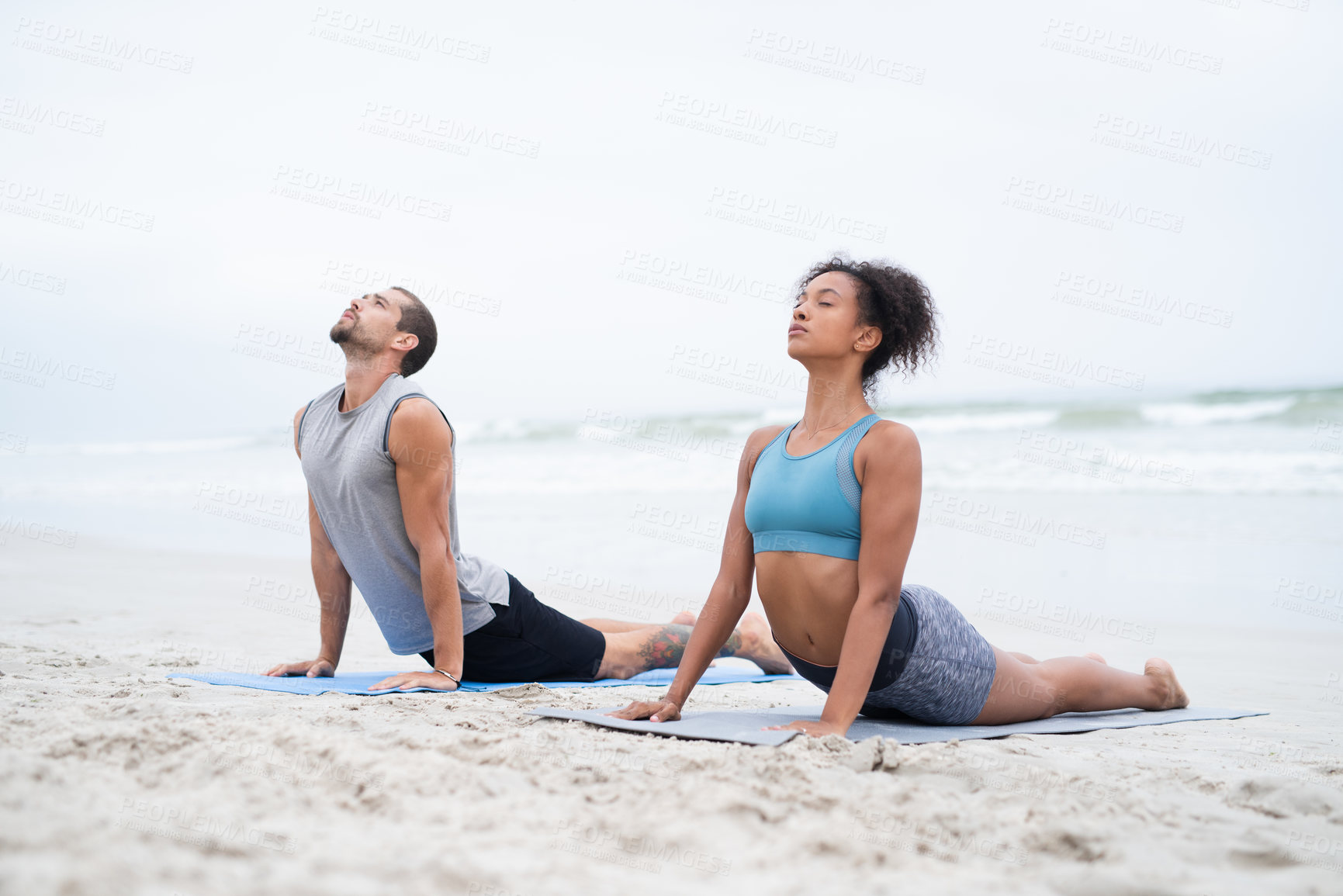 Buy stock photo Shot of a young man and woman practising yoga together at the beach