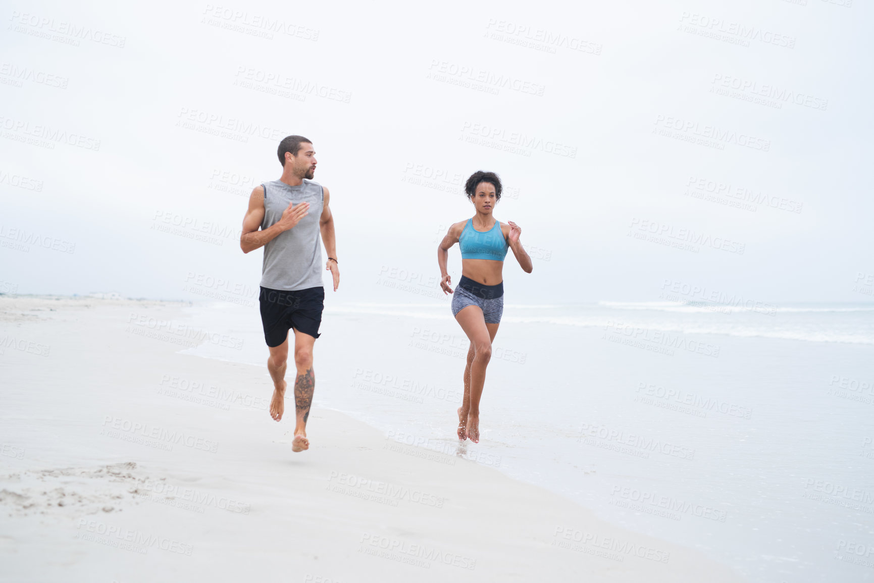 Buy stock photo Shot of a young couple running along the beach together