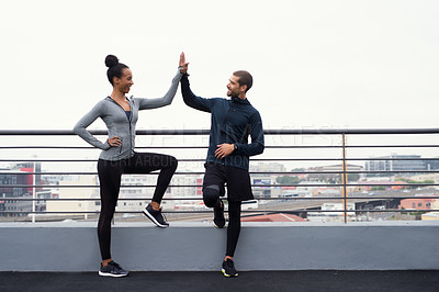 Buy stock photo Shot of a sporty young man and woman giving each other a high five while exercising outdoors