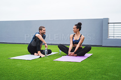 Buy stock photo Shot of a young man and woman taking a break while practising yoga together outdoors