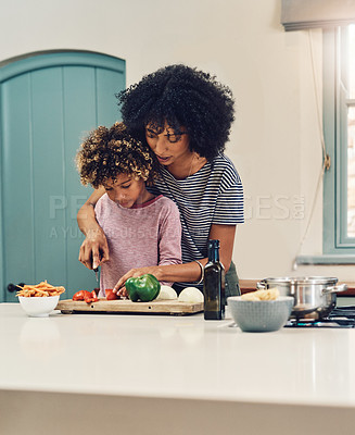 Buy stock photo Shot of a young boy cutting vegetables with the assistance of his mother