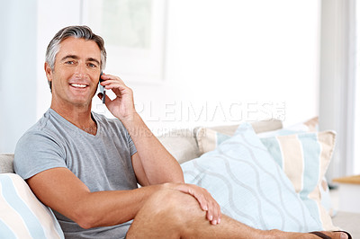 Buy stock photo Cropped portrait of a handsome mature man sitting on his living room sofa alone and talking on his cellphone