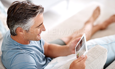 Buy stock photo Cropped shot of a handsome mature man using a tablet while sitting on his living room sofa