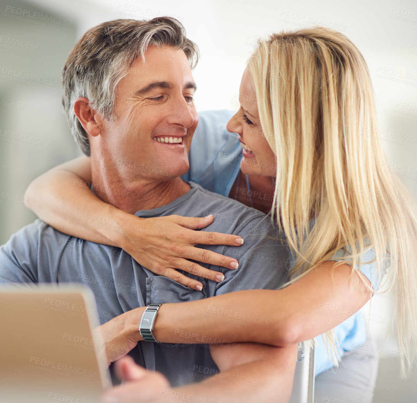 Buy stock photo Cropped shot of an attractive mature woman hugging her handsome mature husband while he uses a laptop in the house