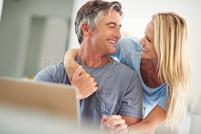 Buy stock photo Cropped shot of an attractive mature woman hugging her handsome mature husband while he uses a laptop in the house