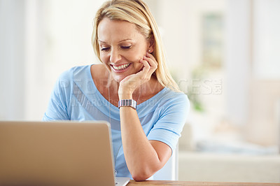 Buy stock photo Cropped shot of an attractive mature woman sitting and using a laptop while in her living room during the day