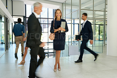 Buy stock photo Full length shot of an attractive young businesswoman standing and holding a tablet while her colleagues walk around her
