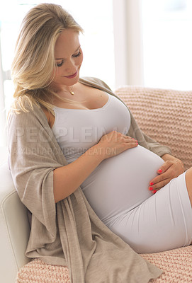 Buy stock photo Cropped shot of an attractive young pregnant woman holding her belly while relaxing on her couch at home