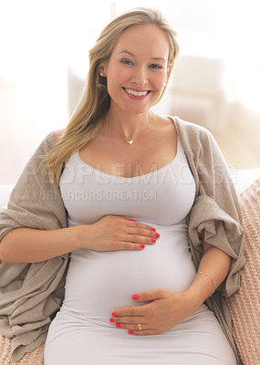 Buy stock photo Cropped portrait of an attractive young pregnant woman holding her belly while relaxing on her couch at home
