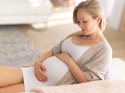 Buy stock photo Cropped shot of an attractive young pregnant woman holding her belly while relaxing on her couch at home