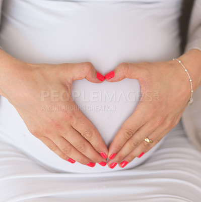 Buy stock photo Closeup shot of an unrecognizable young pregnant woman making a heart shape on her belly at home