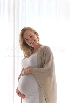 Buy stock photo Cropped portrait of an attractive young pregnant woman holding her belly while standing in her  home