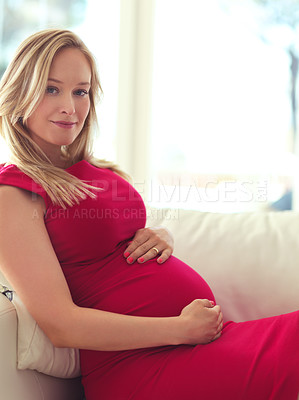 Buy stock photo Cropped portrait of an attractive young pregnant woman holding her belly while relaxing on her couch at home