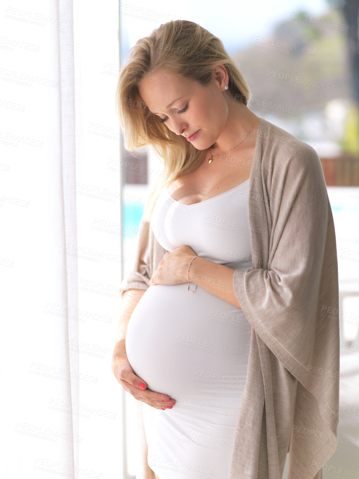 Buy stock photo Cropped shot of an attractive young pregnant woman holding her belly while standing in her home