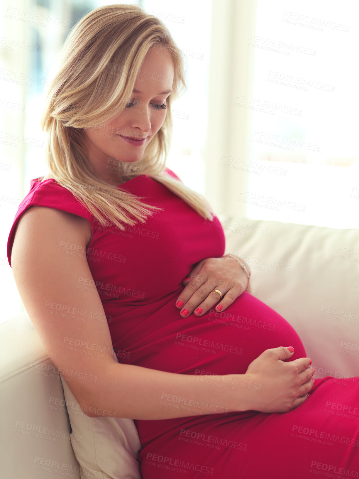 Buy stock photo Cropped shot of an attractive young pregnant woman holding her belly while relaxing on her couch at home