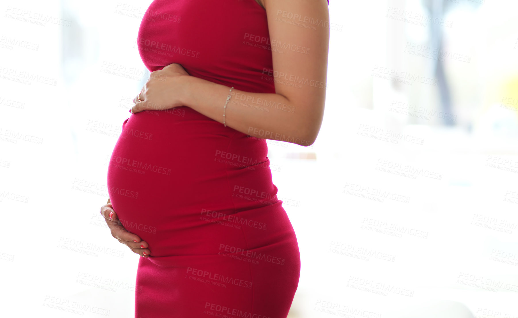 Buy stock photo Cropped shot of an unrecognizable pregnant young woman holding her belly while standing in her home