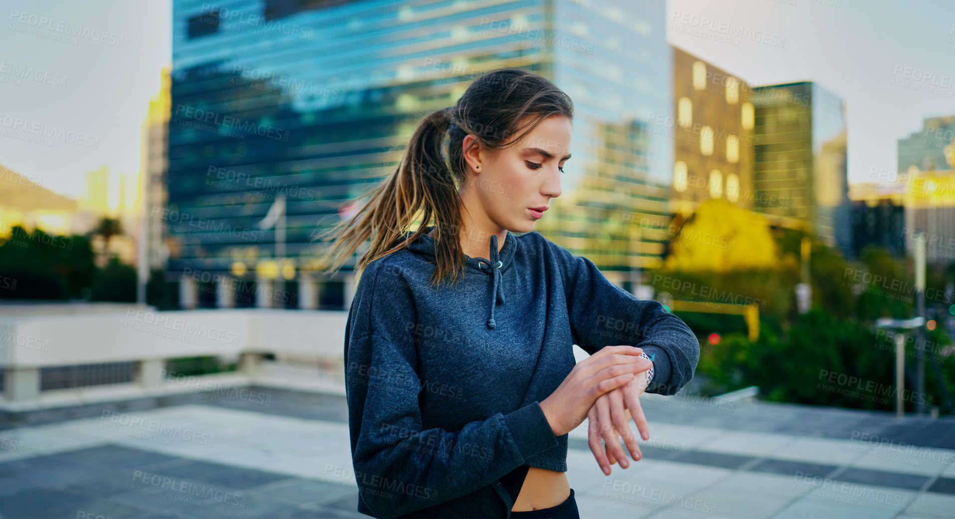 Buy stock photo Shot of a young woman looking at her watch while exercising in the city