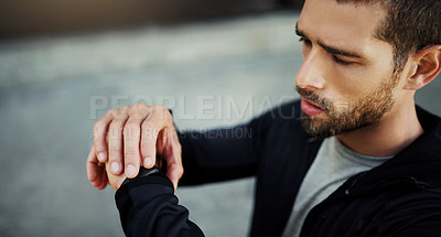 Buy stock photo Shot of a young man looking at his watch while exercising in the city