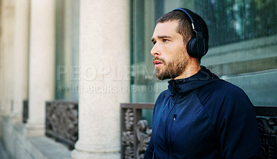 Buy stock photo Shot of a young man listening to music during his workout in the city
