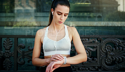 Buy stock photo Shot of a young woman looking at her watch while exercising in the city