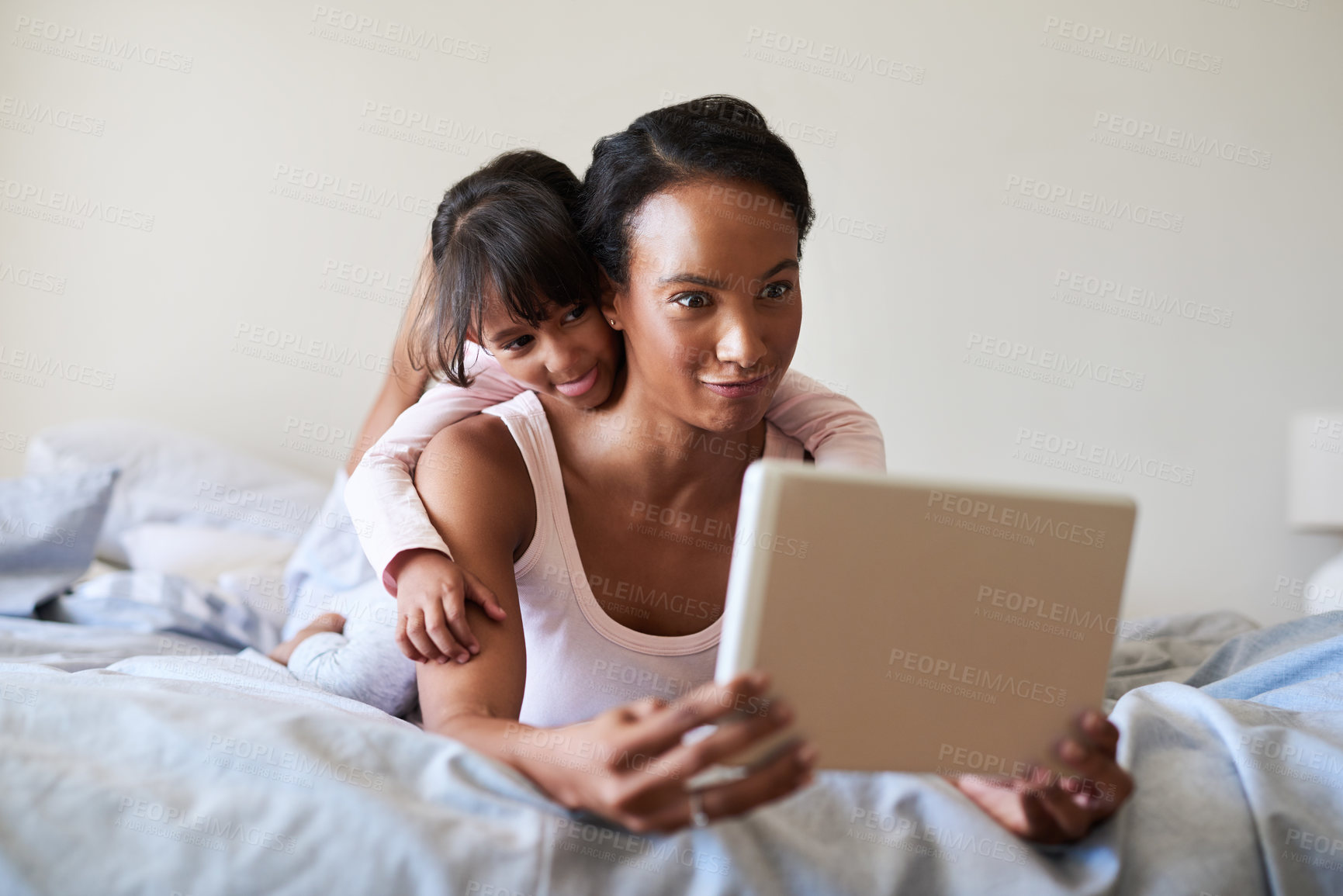 Buy stock photo Shot of a beautiful young mother and daughter using a digital tablet while relaxing in bed together at home