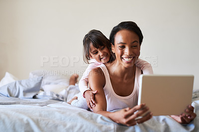 Buy stock photo Shot of a beautiful young mother and daughter using a digital tablet while relaxing in bed together at home