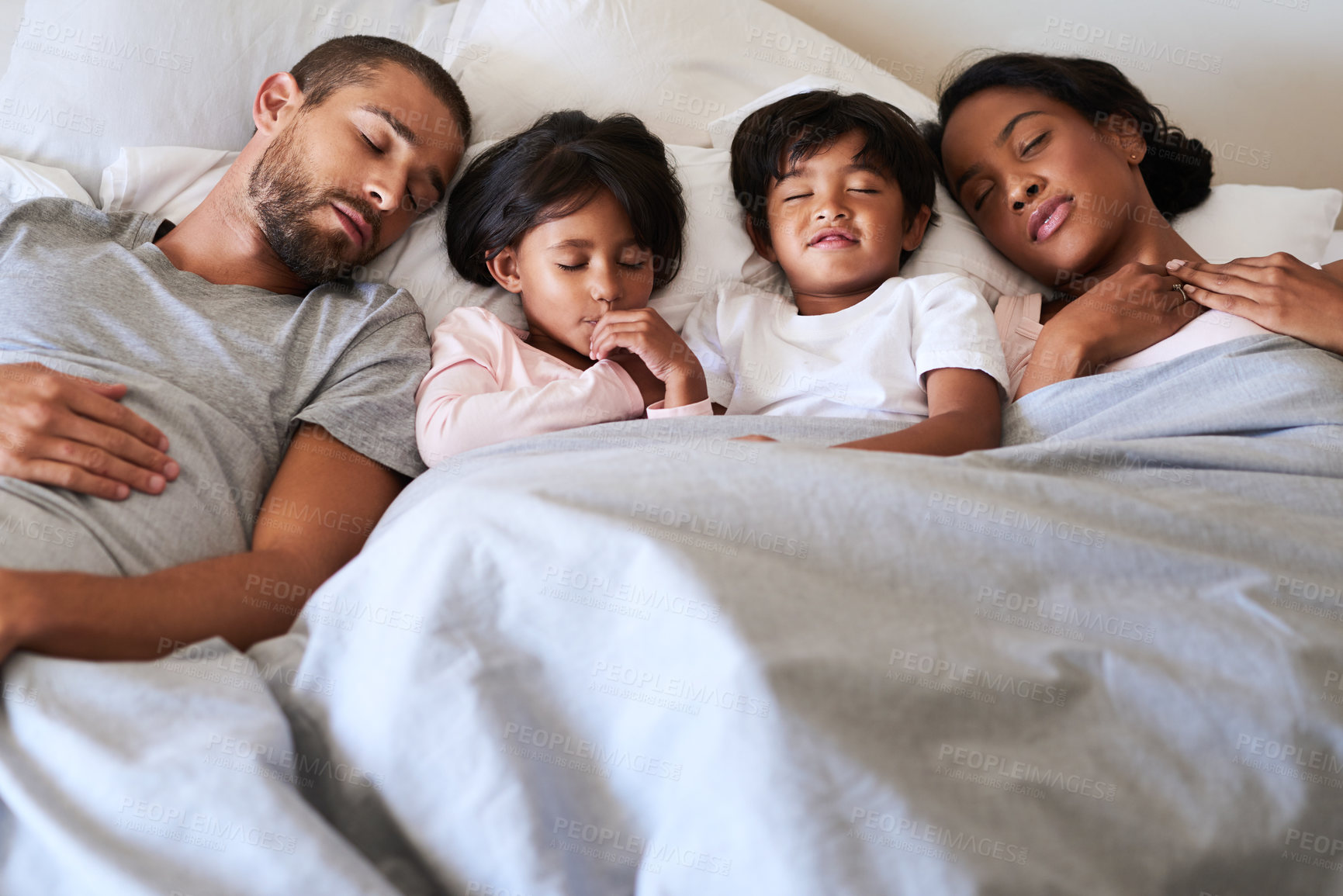 Buy stock photo Shot of a beautiful young family of four fast asleep in bed together in their bedroom at home